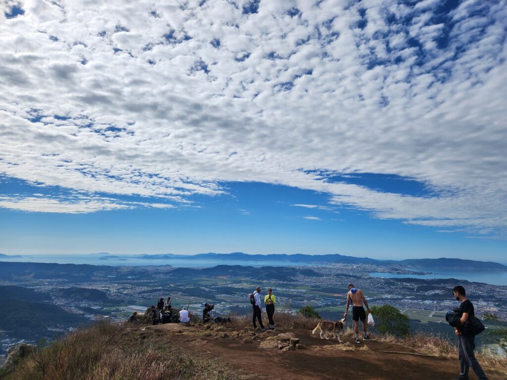 Um grupo de pessoas felizes no topo do Morro da Pedra Branca, celebrando a conquista da trilha com a vista panorâmica.